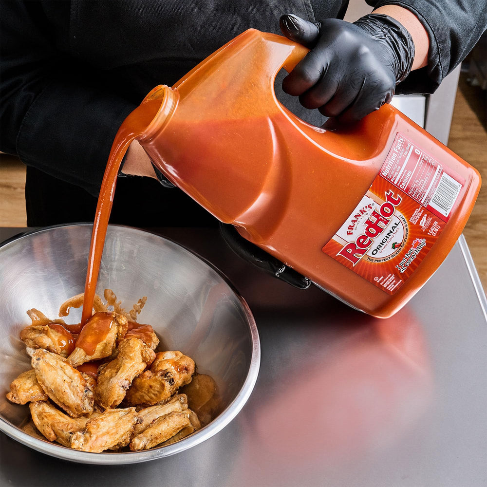 Frank's RedHot galón junto a utensilios para referencia de tamaño