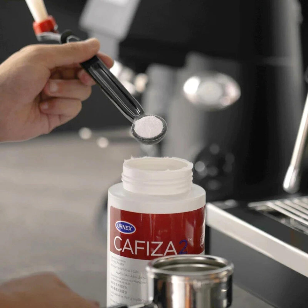 Urnex Cafiza polvo disuelto en agua creando espuma activa para eliminar aceites